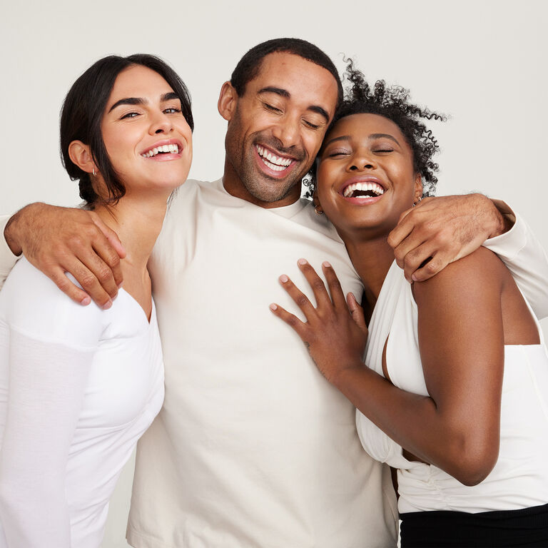 Three people standing close together wearing light-colored tops against a neutral background