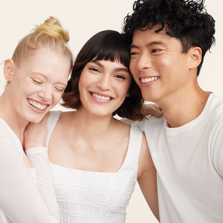 Two women and one man standing close with arms around each other wearing white shirts, Mary Kay.