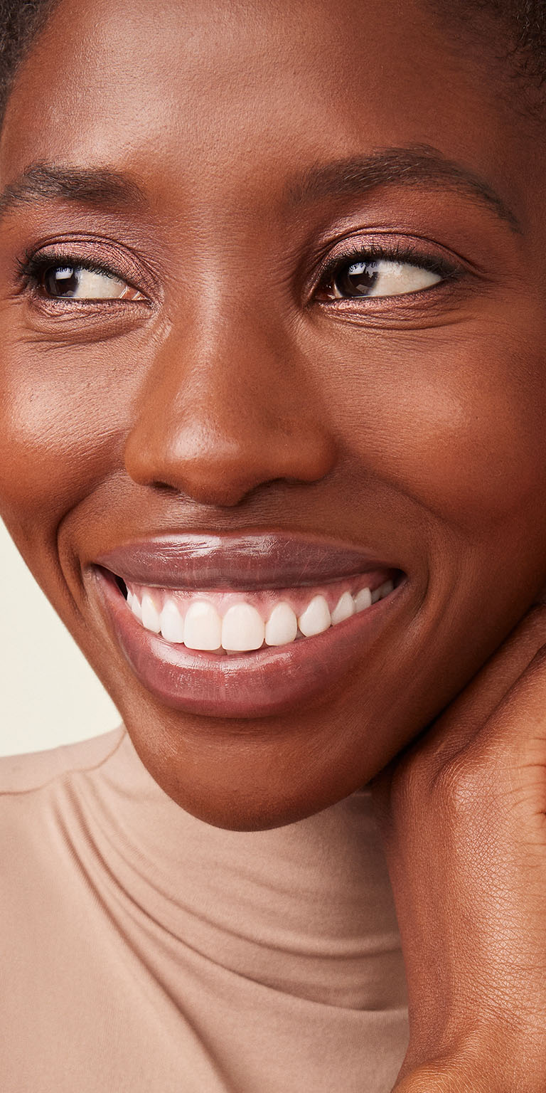 Mujer de piel oscura sonriendo hacia un lado de la c&aacute;mara.